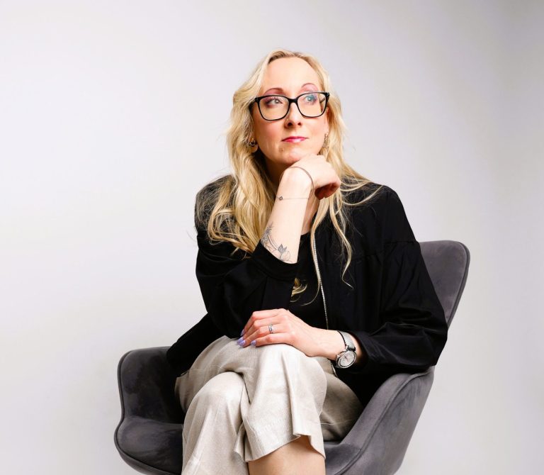 Anna-Susan Franke Leadership Communication Coach Junge Frau mit Brille, lächelnd, in einem hellen Raum, trägt ein Outfit aus Blazer und Jeans.