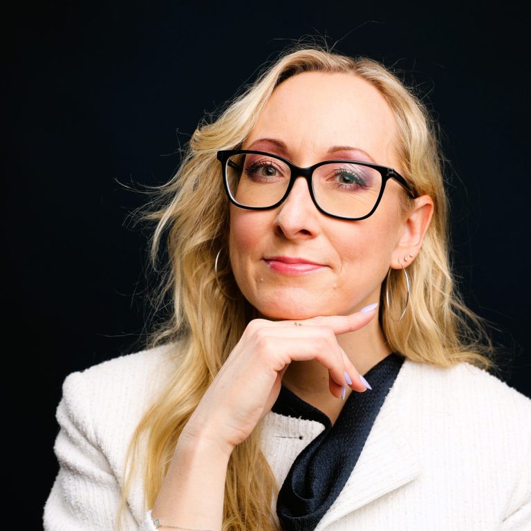 Anna-Susan Franke Leadership Communication Coach Eine Frau mit langen blonden Haaren und Brille, lächelt selbstbewusst.